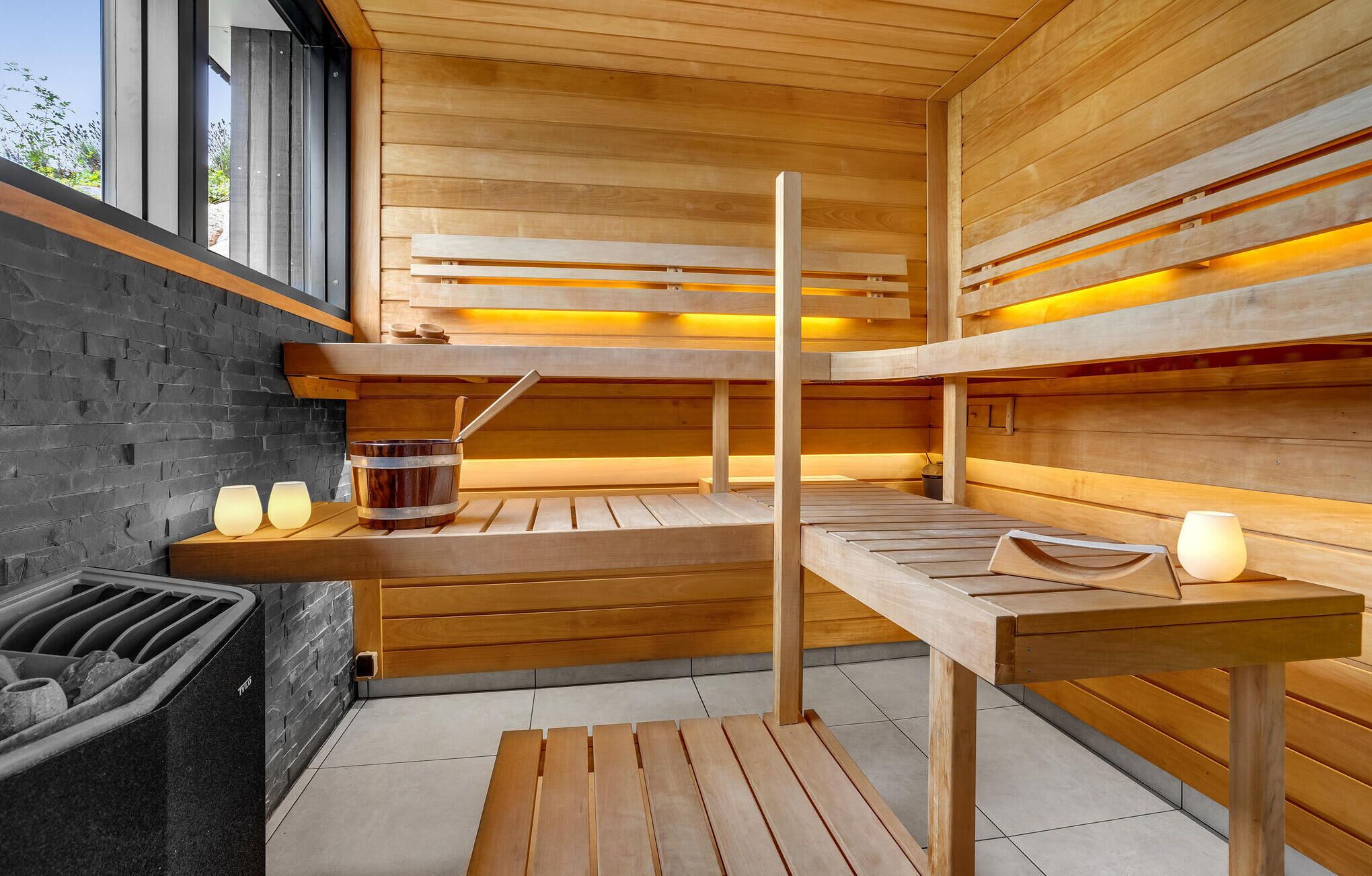 A sauna with wooden benches, a bucket, and wall-mounted lights.