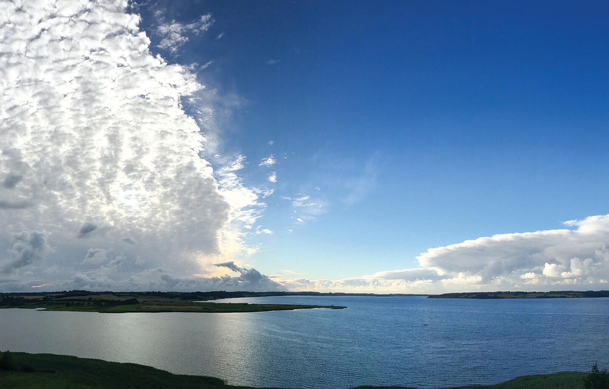 A calm lake with a clear sky and a large cloud formation.