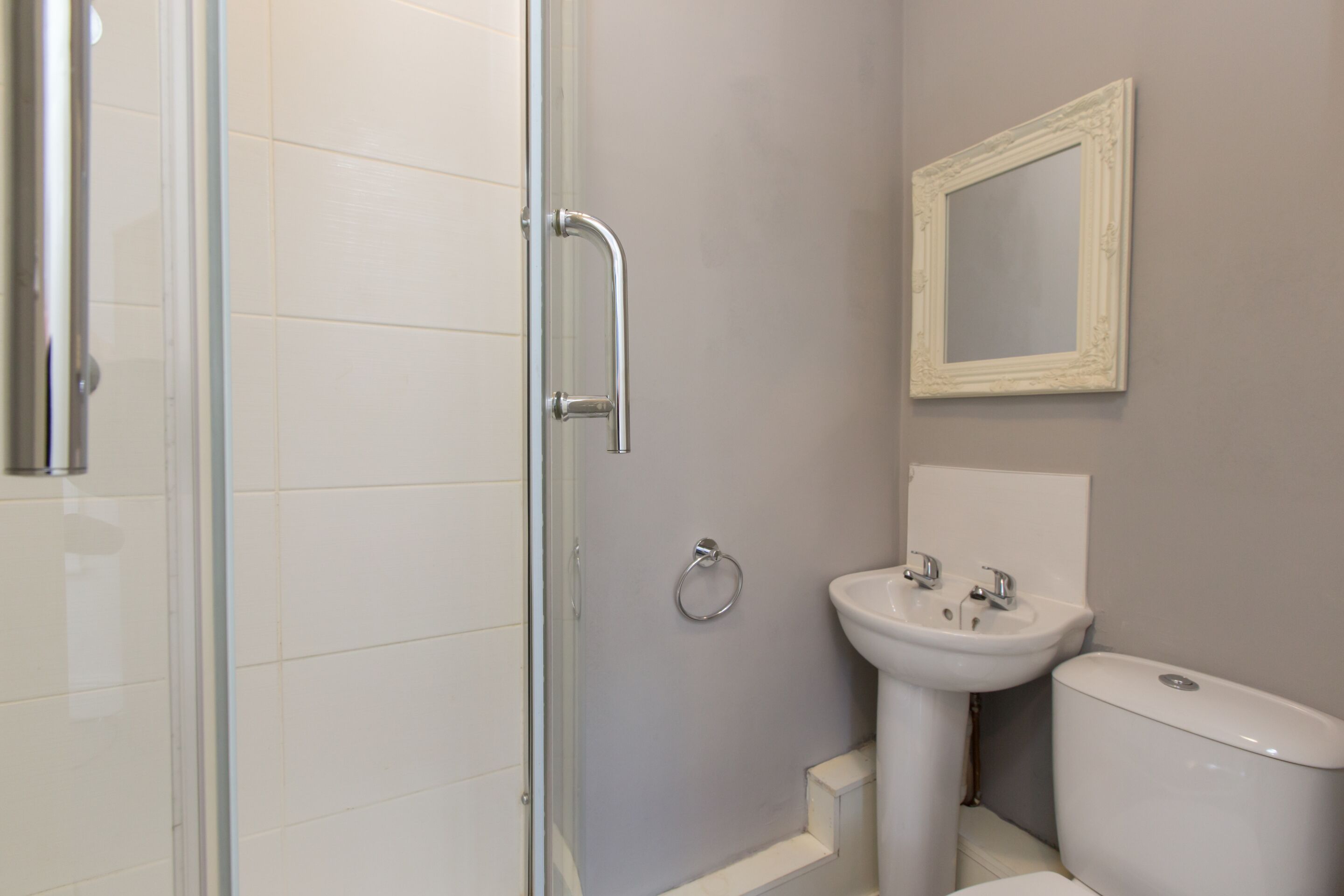 A bathroom with a glass shower enclosure, a sink with a mirror above it, and a toilet.