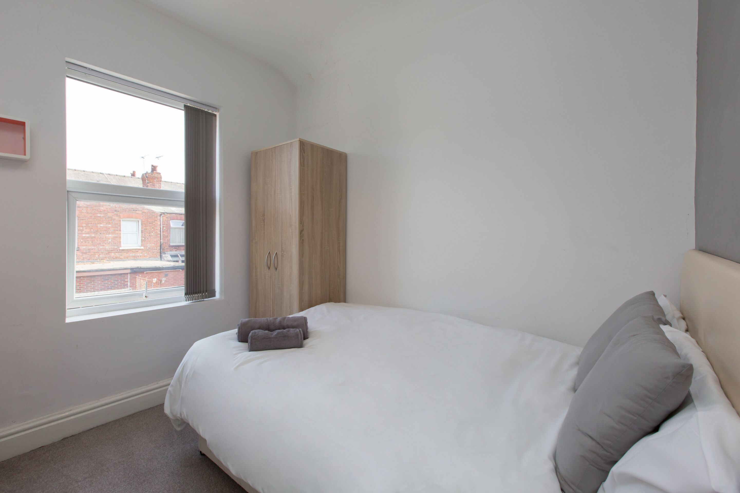 A bedroom with a bed, a wardrobe, and a window with a view of a brick building.