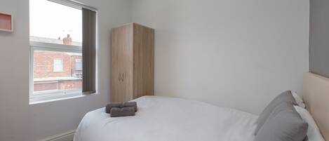 A bedroom with a bed, a wardrobe, and a window with a view of a brick building.