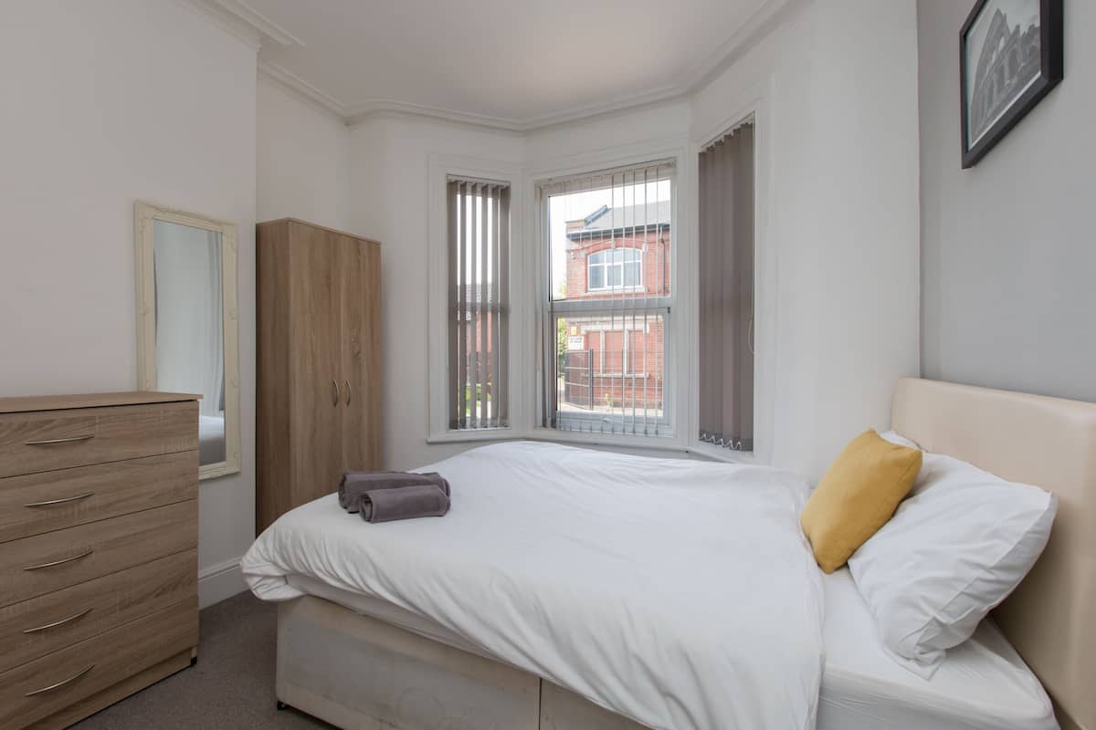 Ein Schlafzimmer mit einem Bett, einem Holzschrank und einem Fenster mit Jalousien.