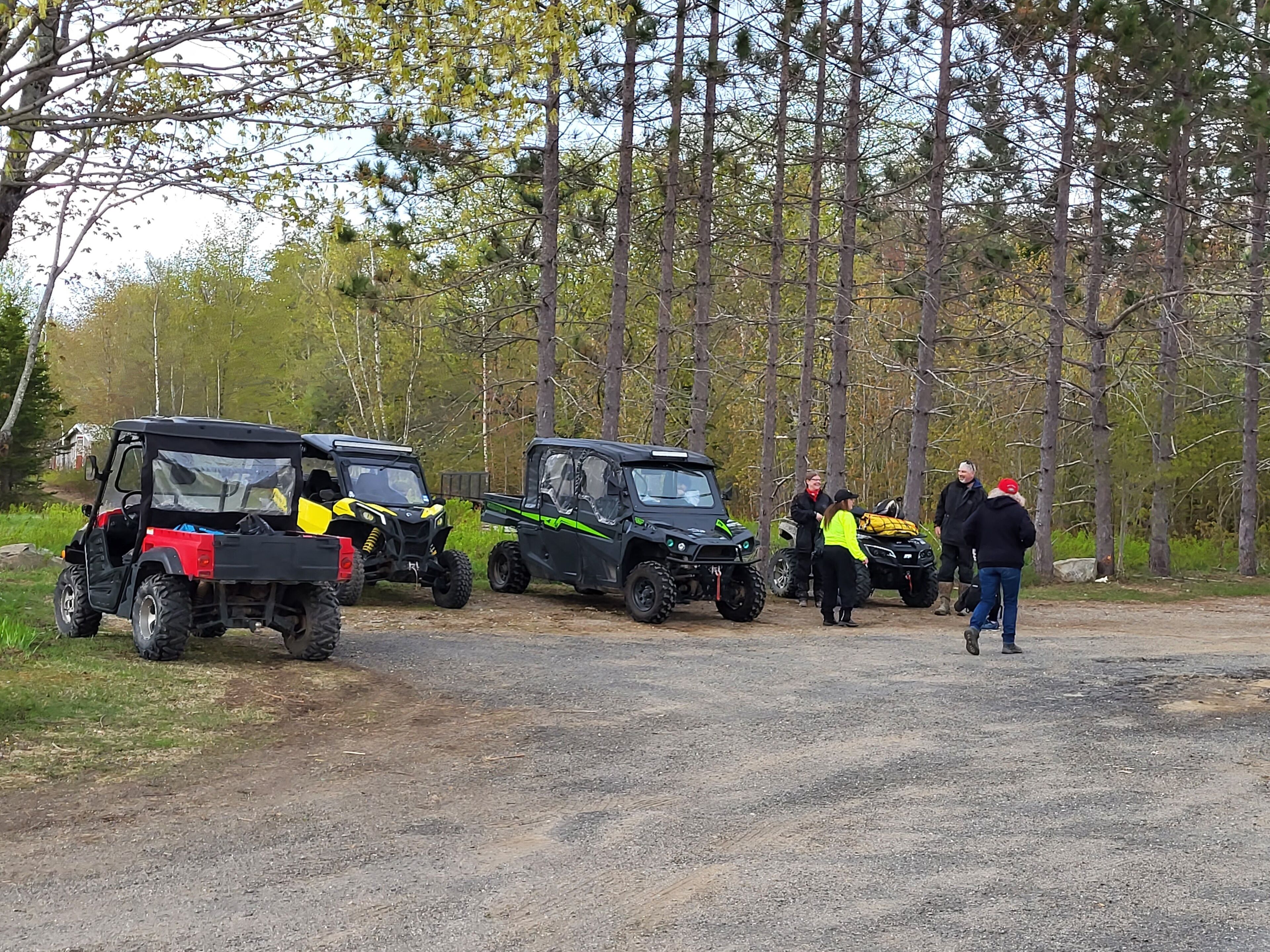A group of off-road vehicles parked on a dirt path in a wooded area.
