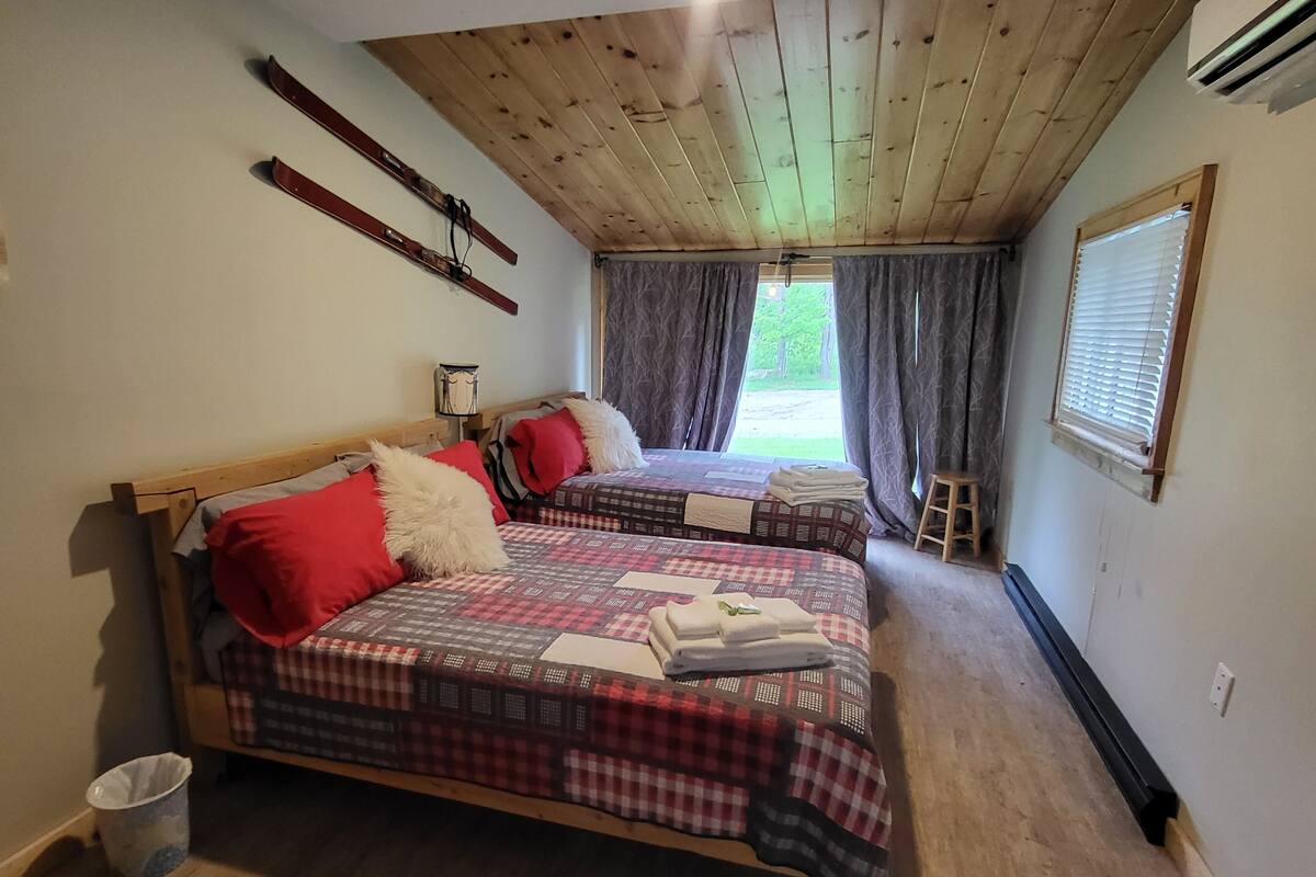 A room with two beds, wooden ceiling, and a window with curtains.