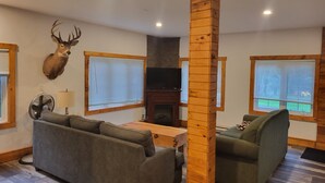 A living room with a sofa, a green armchair, a wooden pillar, a mounted deer head, a fireplace, and a television. - Crabbe Mountain Inn (Central Hainesville)
