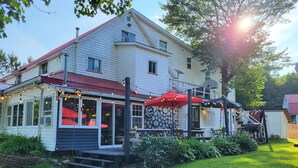 A two-story house with a red roof, a porch with red umbrellas, and a stone wall. - Crabbe Mountain Inn (Central Hainesville)
