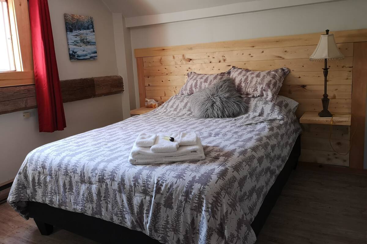 A bed with a forest-themed bedspread, a bedside lamp, and a neatly folded towel on the bed.