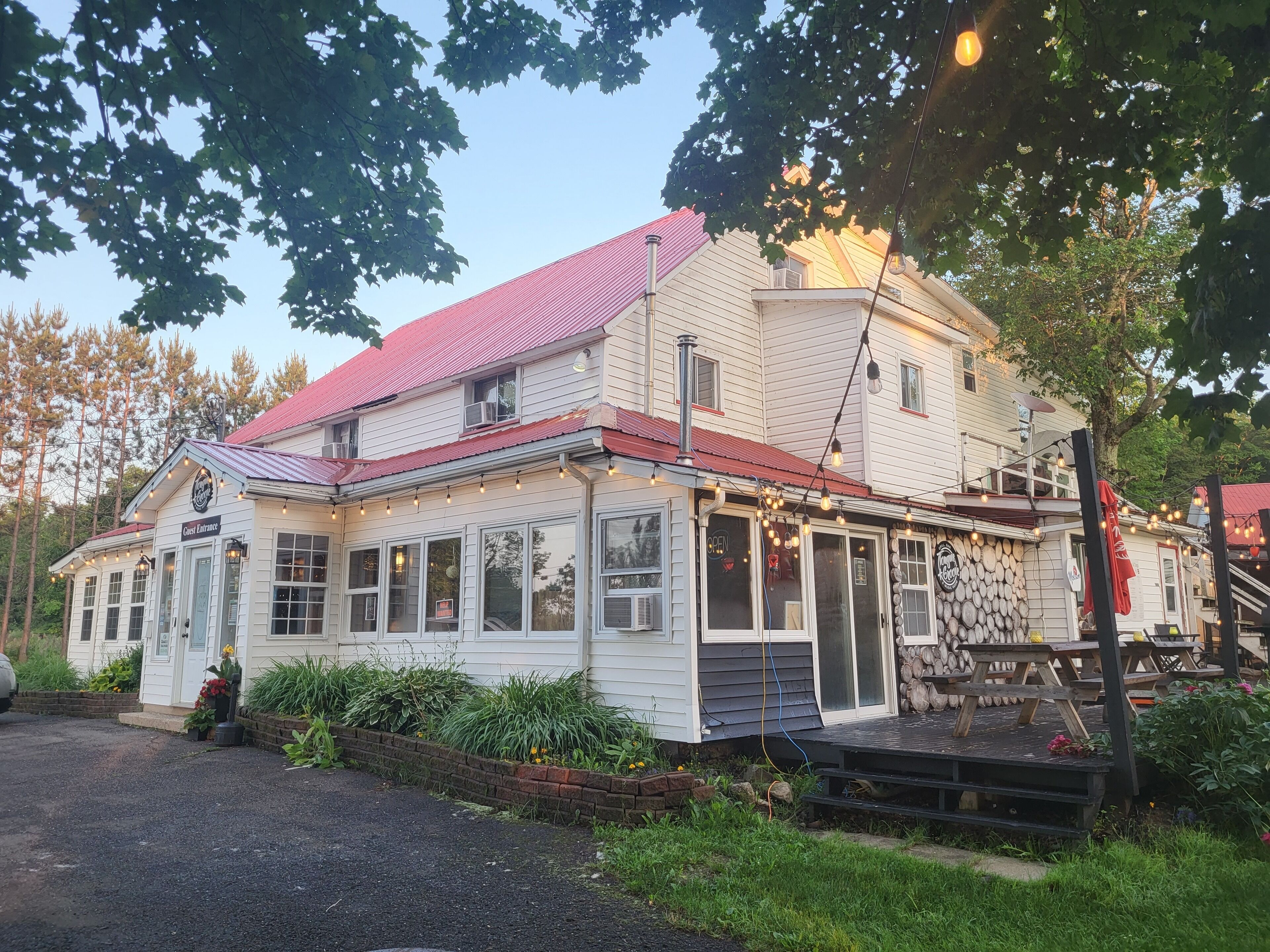A two-story building with a red roof, a porch with benches, and a sign indicating a guest entrance.