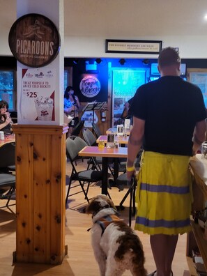 A restaurant interior with wooden furniture, a dog on a leash, and a person in a uniform. - Crabbe Mountain Inn (Central Hainesville)