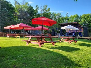 An outdoor event with picnic tables and red umbrellas, a stage with musical equipment, and a Coors Light tent. - Crabbe Mountain Inn (Central Hainesville)