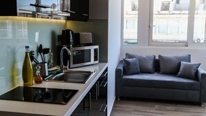 A modern kitchen with a central island, a grey sofa, and large windows. - Triple A - Evripidou 36 (Athens)