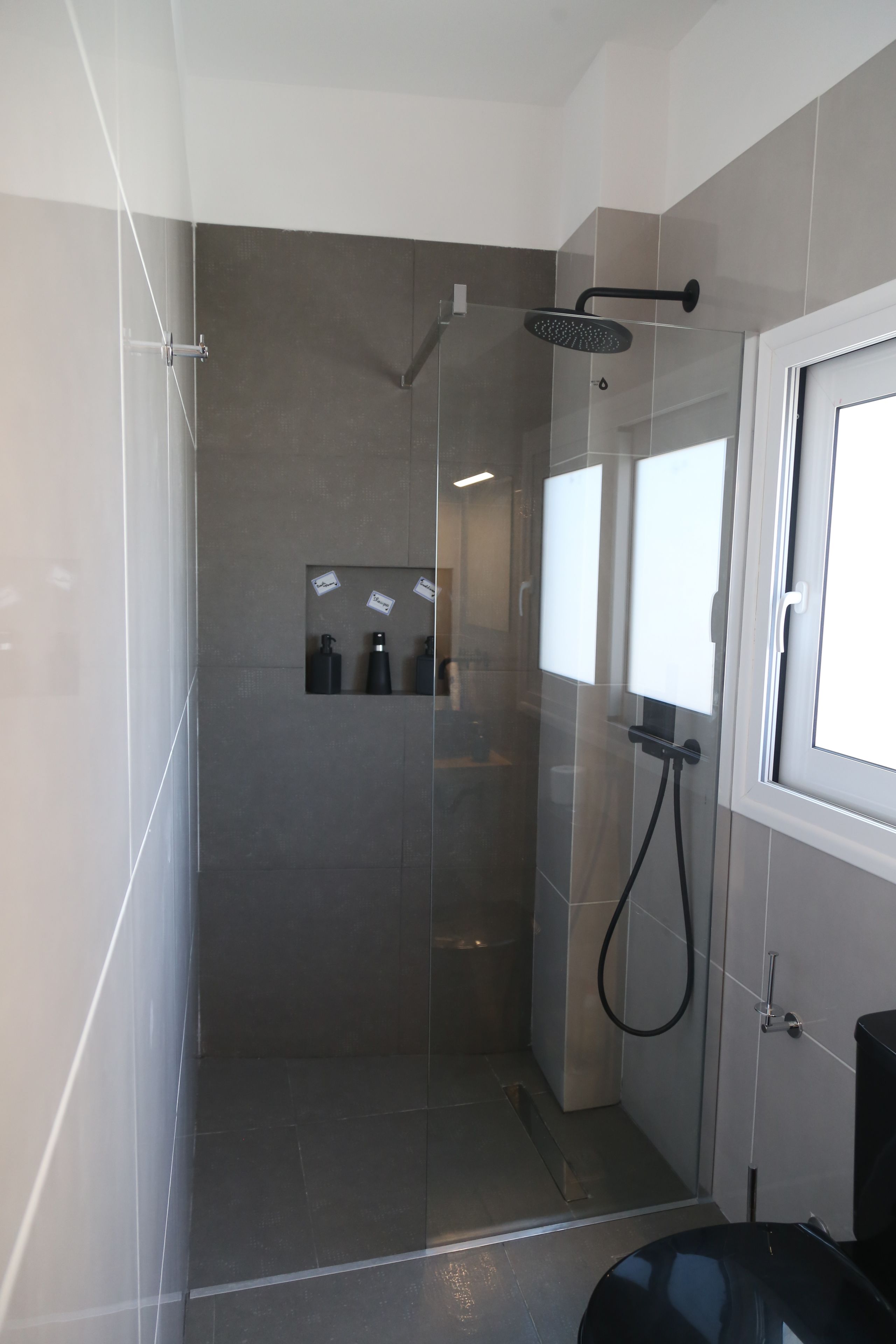 Un espace douche moderne doté d’une porte en verre, d’un pommeau de douche à main et d’un tuyau noir.