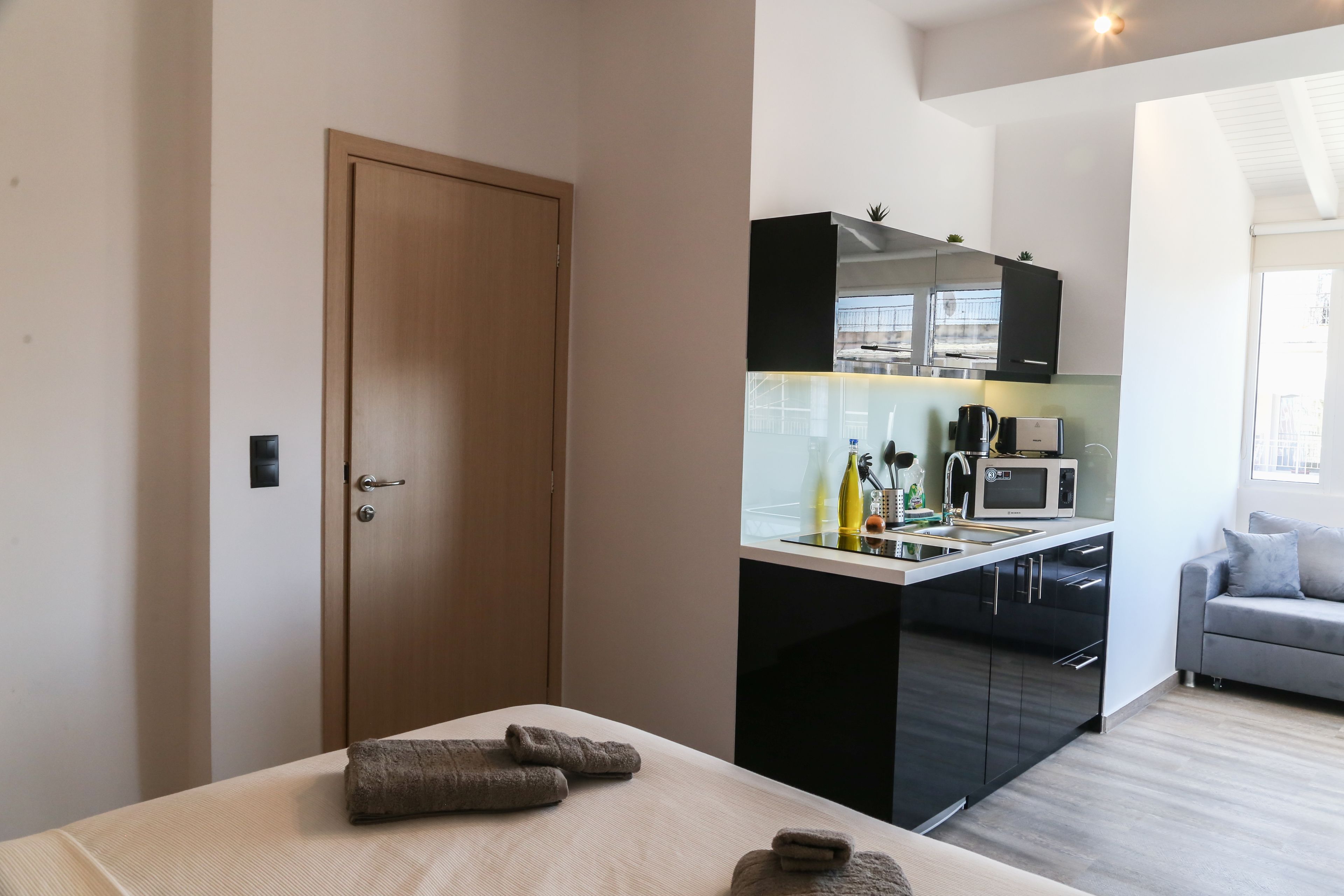 Een moderne kamer met een bed, een houten deur, een kitchenette en een grijze bank.
