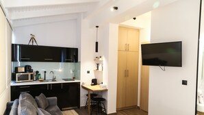 A modern room with a sofa, a small kitchen area, a wooden cabinet, and a TV mounted on the wall. - Triple A - Evripidou 36 (Athens)