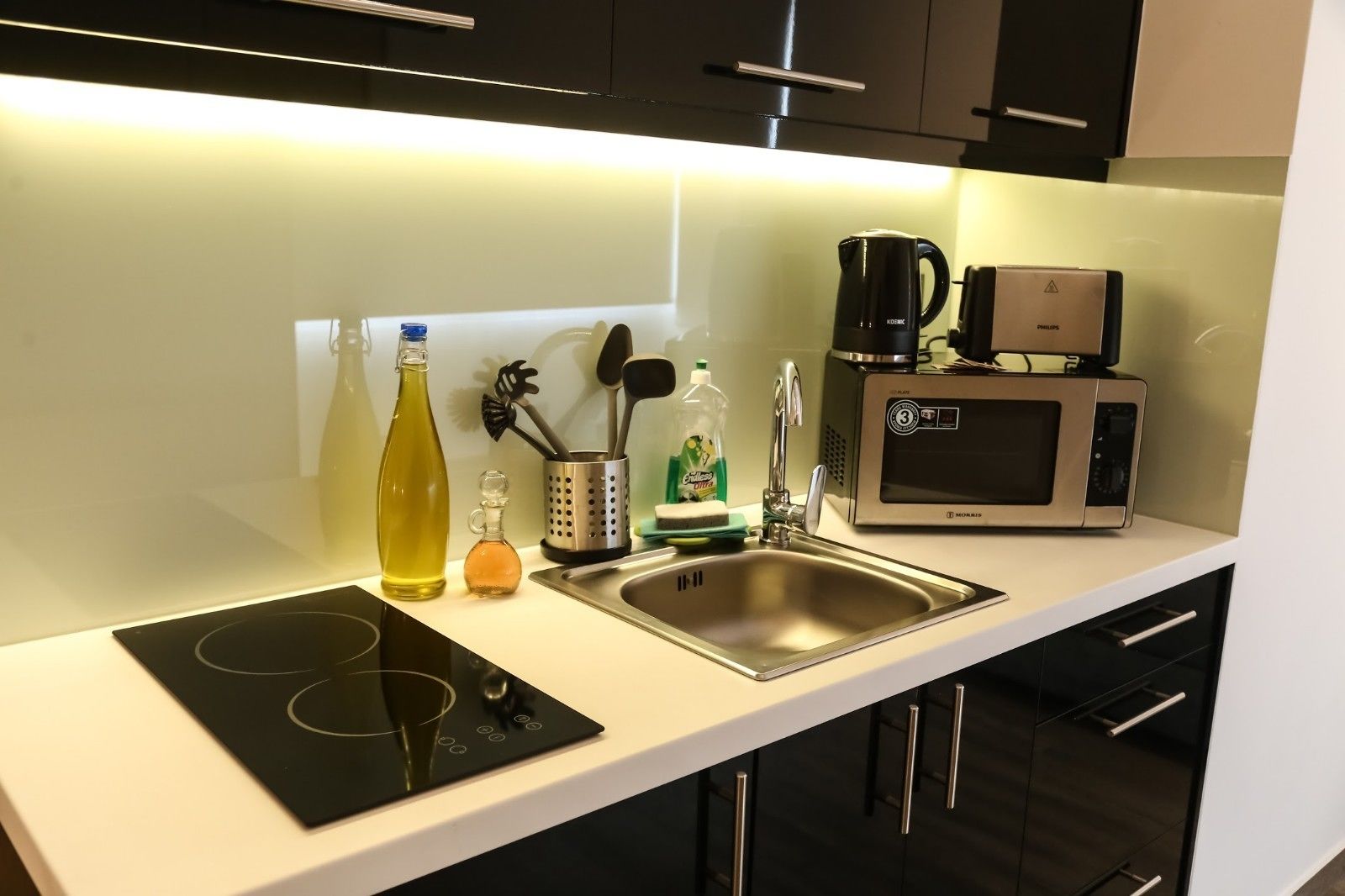 A modern kitchen with a built-in induction cooktop, a stainless steel sink, a microwave, and a coffee maker.