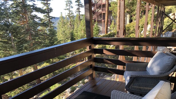 Une terrasse en bois, meublée de meubles en osier, et un paillasson noir.
