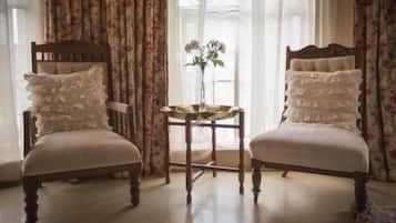 Two upholstered chairs with ruffled pillows, a small round table with a vase, and curtains with a floral pattern.