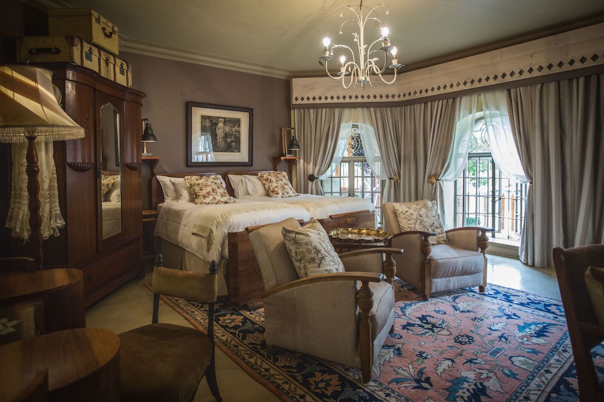Une chambre à coucher de style traditionnel, avec un grand lit, deux fauteuils, une armoire en bois et un lustre.
