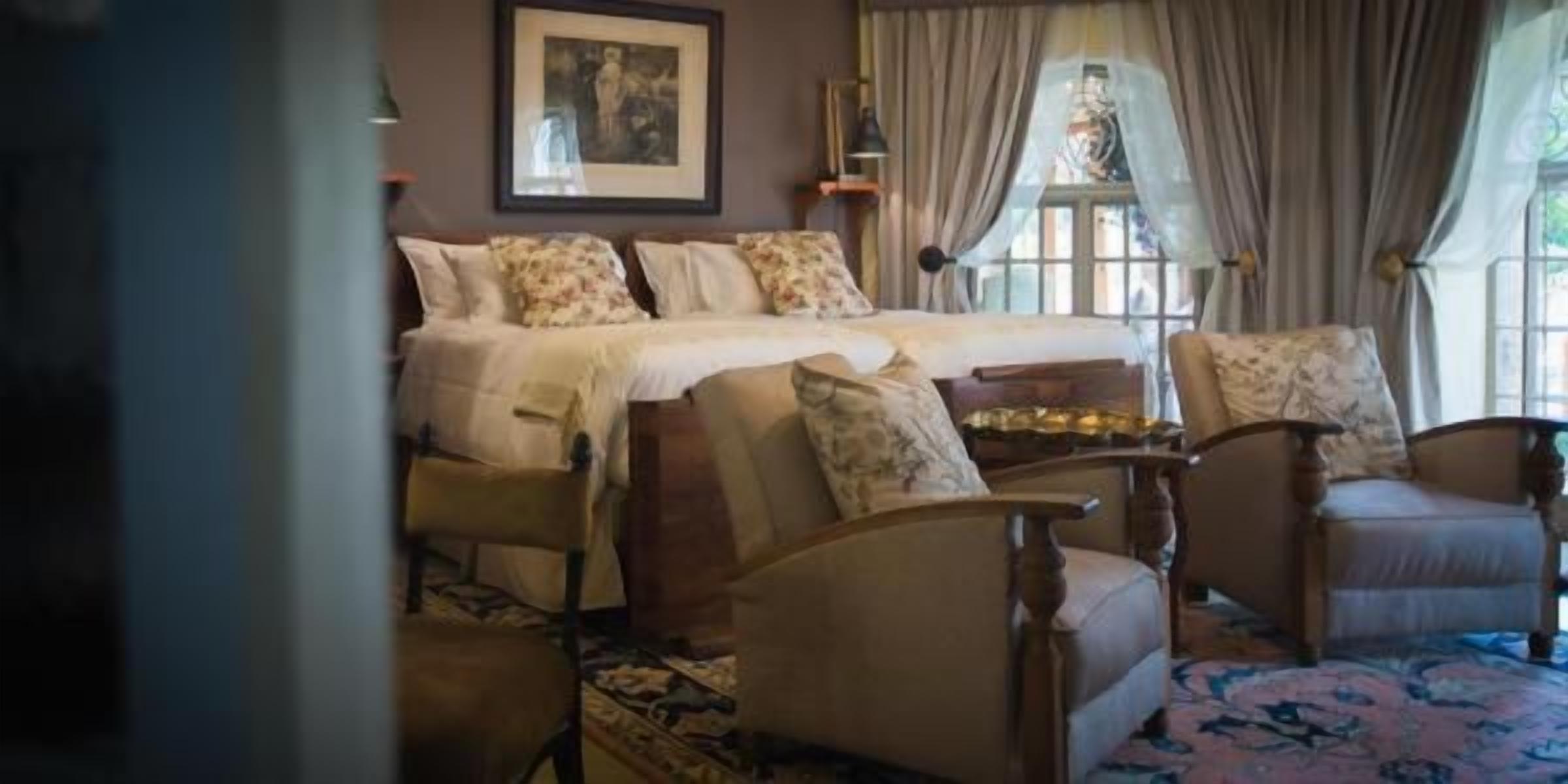 A bedroom with a bed, two chairs, a nightstand, and a window with curtains.