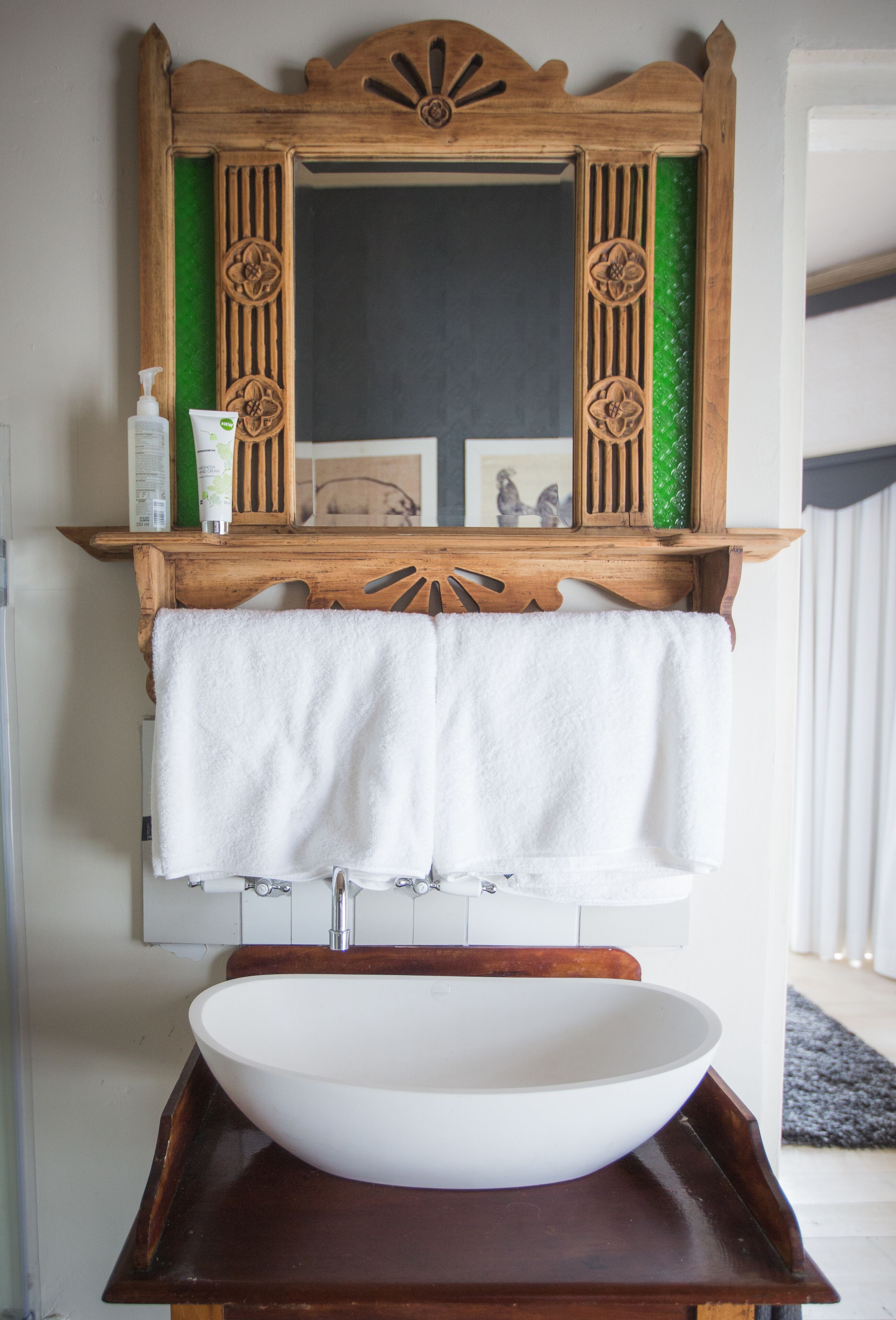 A bathroom with a wooden vanity, a white sink, and a mirror with decorative carvings.