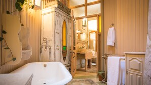 Une salle de bain au style rétro, avec une baignoire sur pieds, un miroir doté d’un cadre décoratif et un meuble-lavabo en bois muni d’un porte-serviettes.