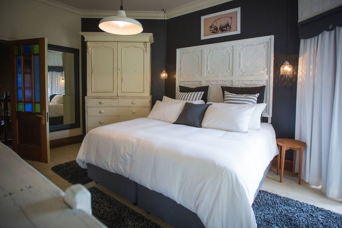 Une chambre avec un grand lit, une commode, un miroir et une fenêtre avec des rideaux.
