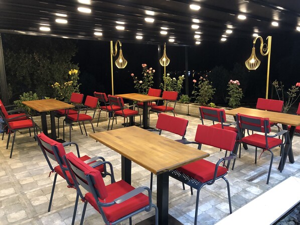 An outdoor dining area with multiple wooden tables and red chairs, surrounded by potted plants and flowers. - Akyaka - Akbuk Fullmoon Bungalow Camping (Mugla)