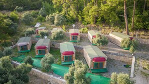 A row of small, wooden cabins with green roofs and red awnings, surrounded by trees and a stone wall.