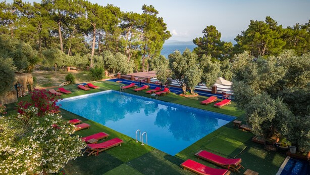 A rectangular pool with red lounge chairs and a small poolside area with a table and chairs.