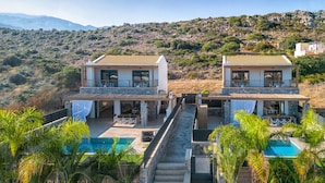 A two-story villa with a swimming pool, outdoor seating, and a view of the surrounding hills. - Villa Calma (Agios Nikolaos)