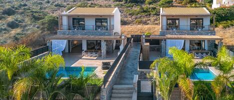 A two-story villa with a swimming pool, outdoor seating, and a view of the surrounding hills.