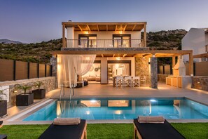 Una casa de dos pisos con piscina, mobiliario exterior y vistas a las colinas.