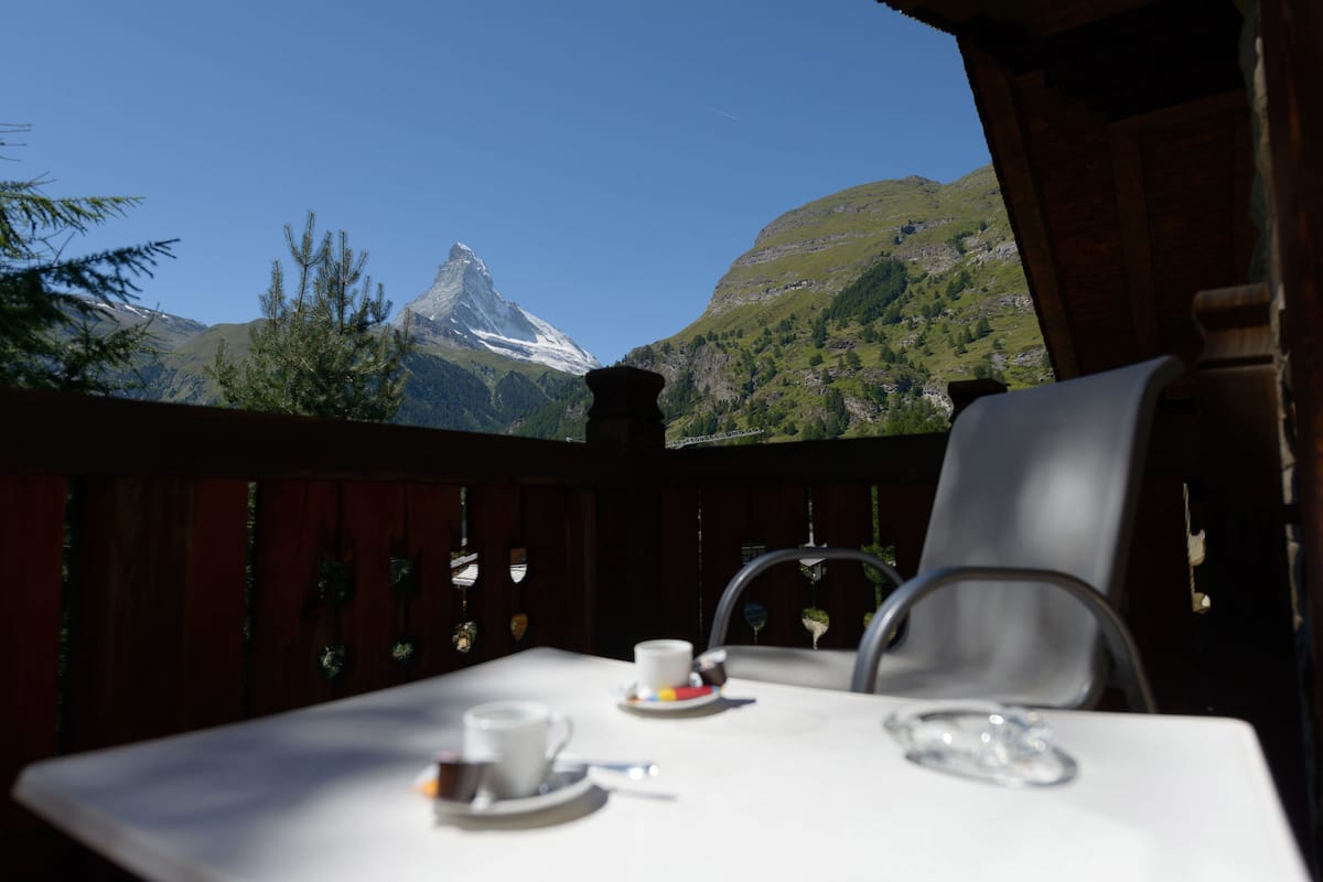 A table with a cup and saucer, a chair, and a view of a mountain.