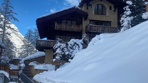 A snow-covered mountain lodge with a stone facade, wooden balconies, and a clear blue sky. - Chalet Kisseye by Zermatt Premium Apartments (Zermatt)