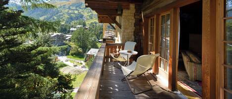 A wooden deck with a view of a mountainous landscape, a chair, and a small table.