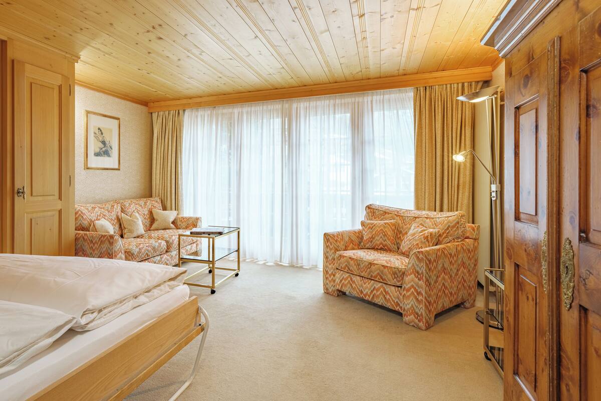 A hotel room with a bed, two armchairs, a small table, and a large window with curtains.