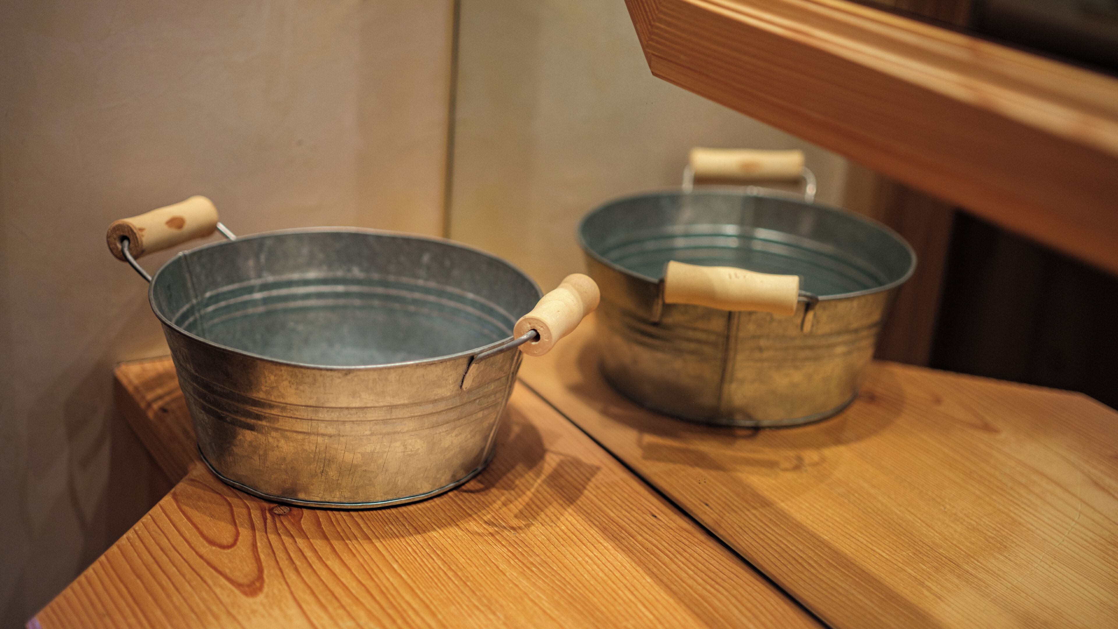 Two metal buckets with wooden handles on a wooden surface.