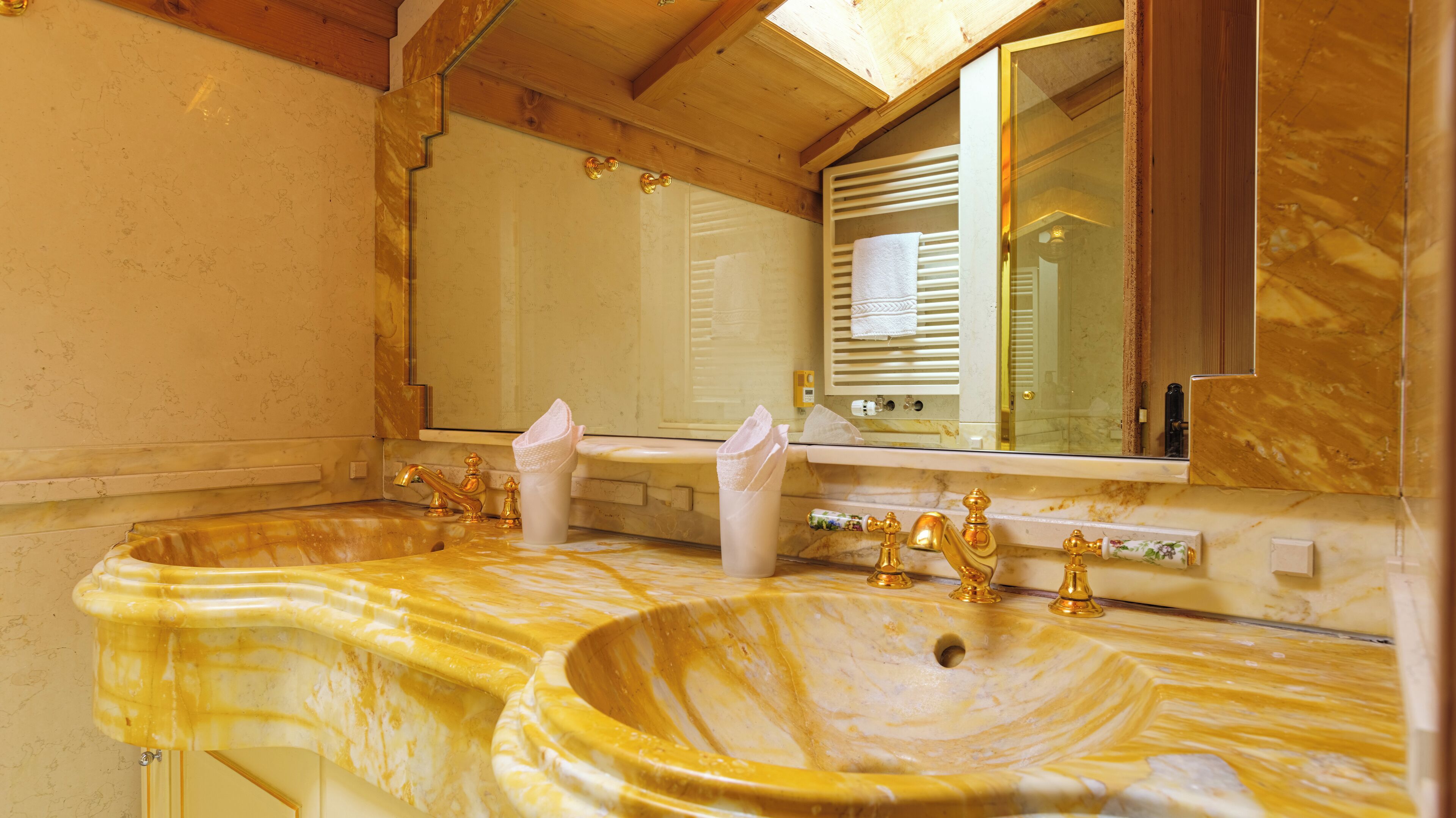 Een badkamer met twee marmeren wastafels, gouden kraanwerk en een grote spiegel.