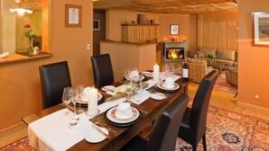A dining room with a long wooden table set for a meal, a fireplace, and a cozy seating area with a patterned rug. - Chalet Kisseye by Zermatt Premium Apartments (Zermatt)