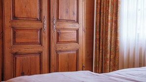 A wooden wardrobe with a handle, a bed with white bedding, and a window with patterned curtains. - Chalet Kisseye by Zermatt Premium Apartments (Zermatt)
