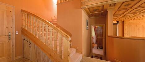 A wooden staircase with a handrail, wooden walls, and a ceiling with exposed beams.