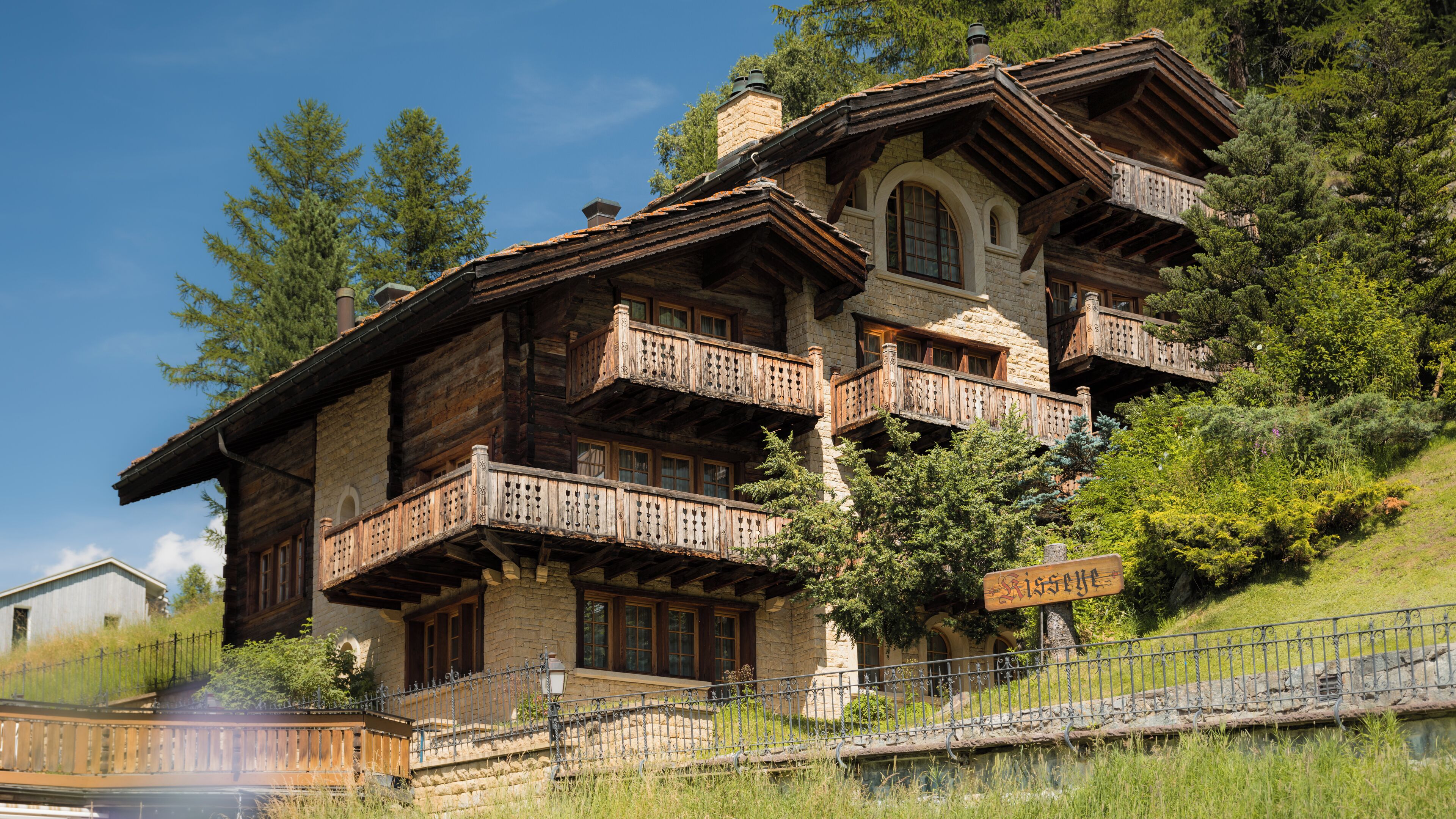 A traditional chalet with multiple balconies, stone walls, and a sign indicating 'Gisella'.