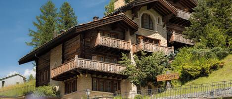 A traditional chalet with multiple balconies, stone walls, and a sign indicating 'Gisella'.