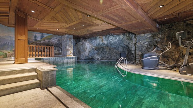 An indoor swimming pool with clear water, stone walls, and exercise equipment. - Chalet Kisseye by Zermatt Premium Apartments (Zermatt)