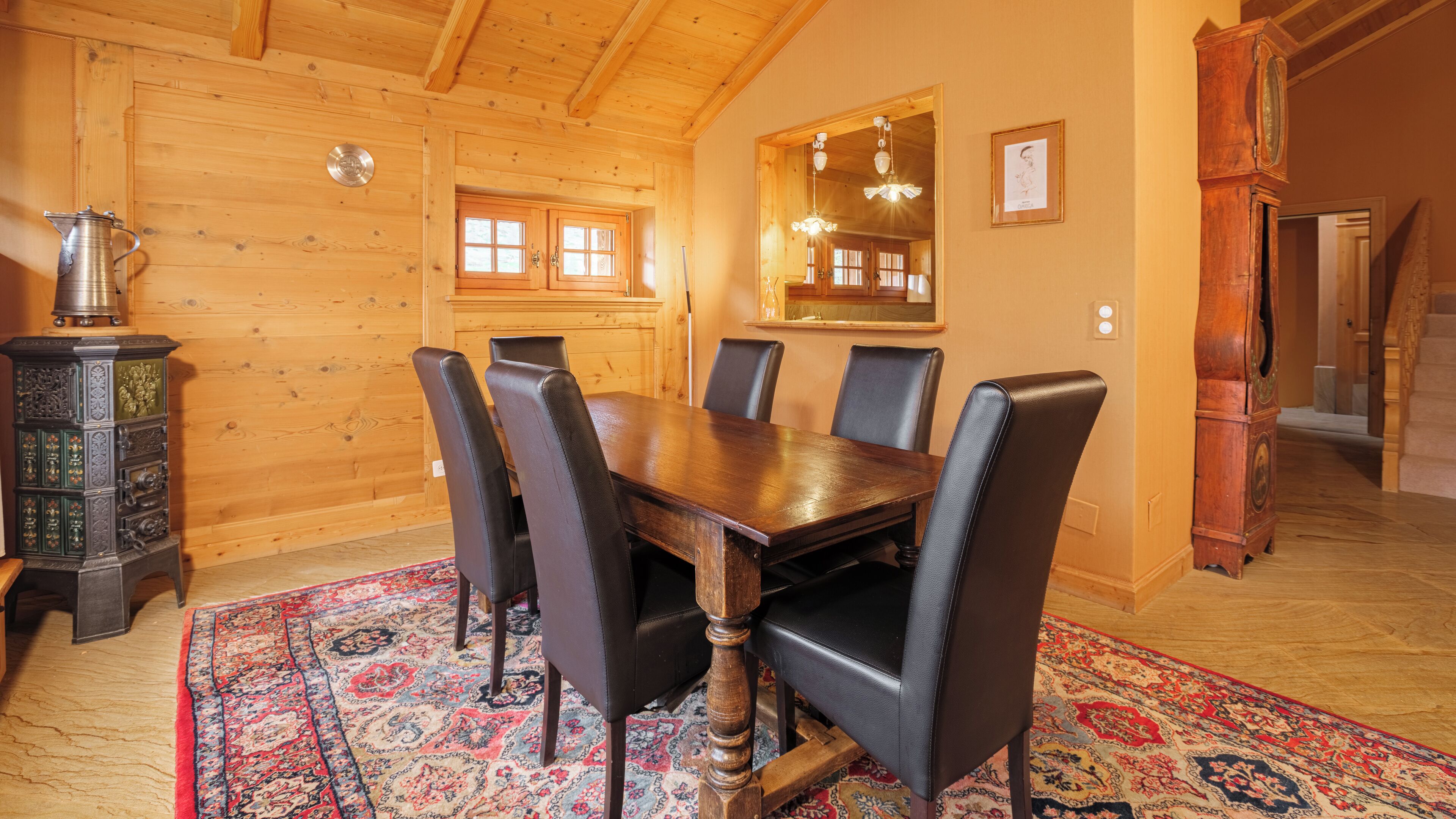 A wooden-paneled dining room with a large table and chairs, a vintage stove, and a patterned rug.