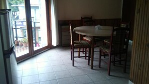 A dining area with a round table and chairs, a refrigerator, and a window with a view of buildings outside. - Departamentos MTD (Balcarce)