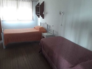 A room with two beds, a window with curtains, a bedside table, and a wall-mounted shelf. - Departamentos MTD (Balcarce)