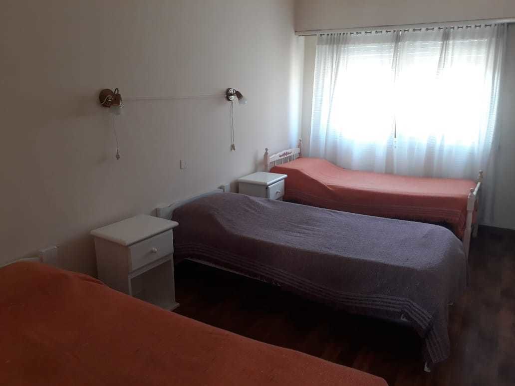 Una habitación con dos camas, una mesita de noche, una pequeña mesa y una ventana con cortinas.