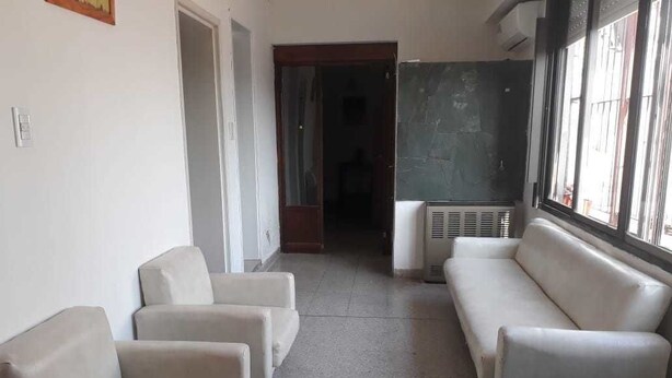 A hallway with two beige sofas, a white door, and a window with blinds. - Departamentos MTD (Balcarce)