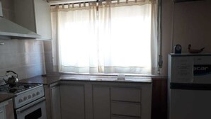A kitchen with white cabinets, a stove, a refrigerator, and a window with sheer curtains. - Departamentos MTD (Balcarce)